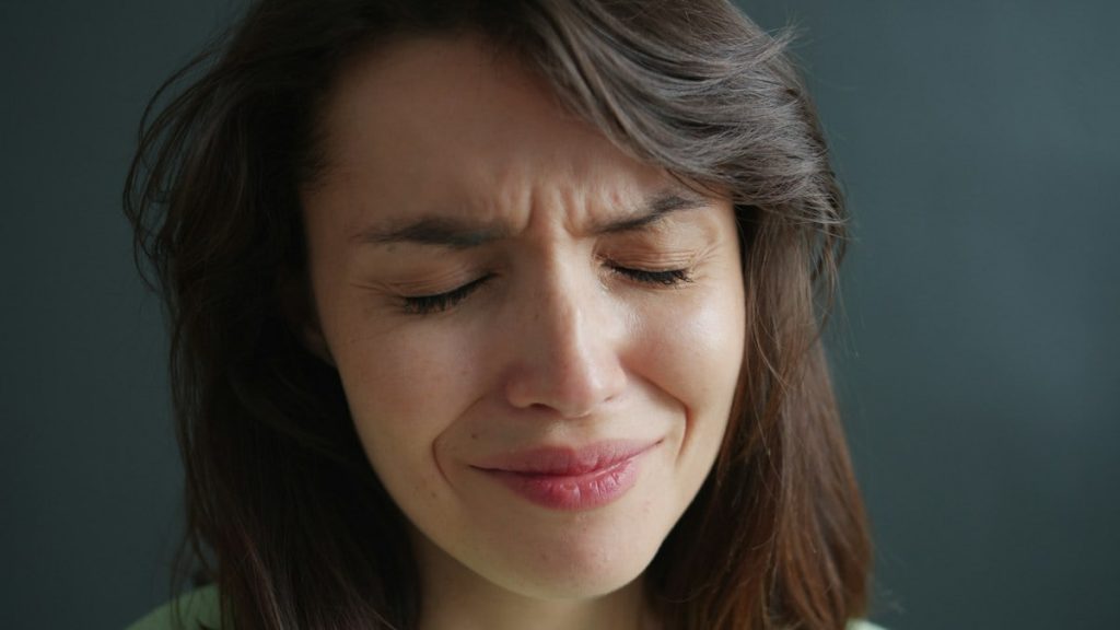 Close-up portrait of unhappy young woman brunette crying feeling sad on dark background. Devastated people, negative emotions and sadness concept.