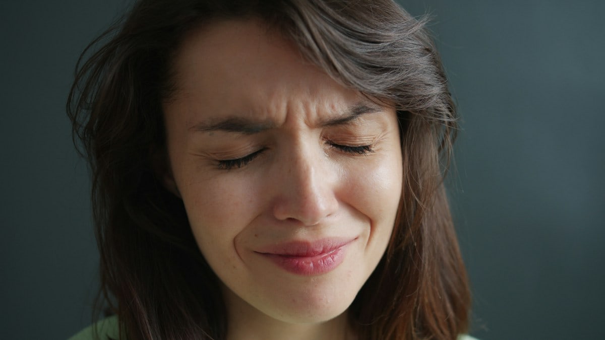 Close-up portrait of unhappy young woman brunette crying feeling sad on dark background. Devastated people, negative emotions and sadness concept.